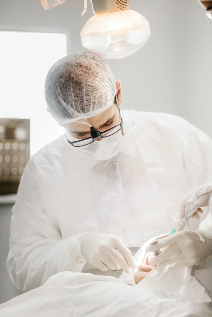 En tandläkare eskilstuna i personlig skyddsutrustning utför ett tandingrepp på en patient, med hjälp av en borr, under starkt undersökningsljus.