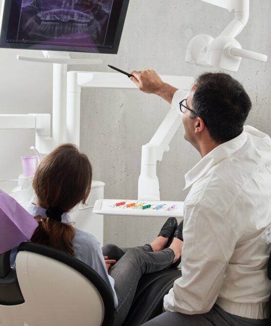 En privata tandläkare Eskilstuna pekar på en tandröntgen på en monitor samtidigt som han förklarar den för en sittande patient i tandklinikens lugna miljö.