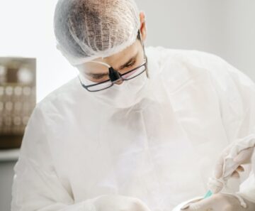 En tandläkare eskilstuna i personlig skyddsutrustning utför ett tandingrepp på en patient, med hjälp av en borr, under starkt undersökningsljus.