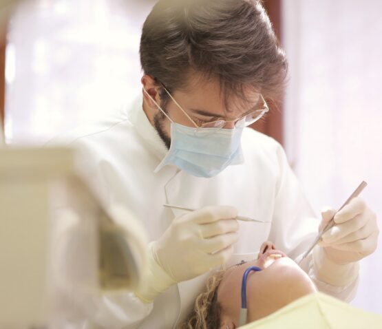 En privata tandläkare eskilstuna, iklädd mask och handskar, undersöker en patients mun med tandverktyg i en orörd klinikmiljö.