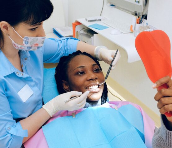 En tandläkare med skyddsutrustning undersöker en leende patient som håller i en orange spegel på en tandvårdsklinik och visar upp den expertvård som privata tandläkare Eskilstuna tillhandahåller.