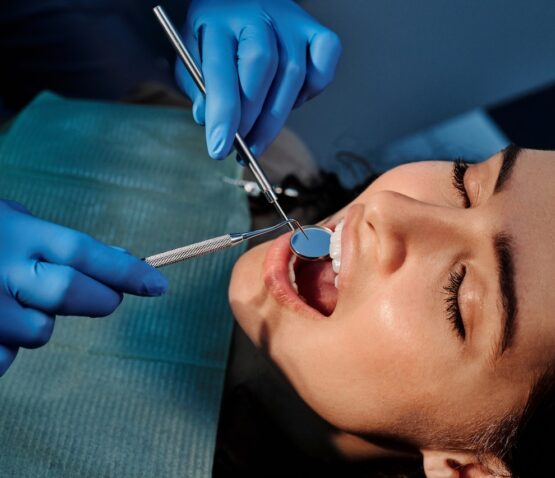 En kvinna med öppen mun, som får sina tänder undersökta av en tandläkare Eskilstuna iklädd blå handskar och med tandverktyg.